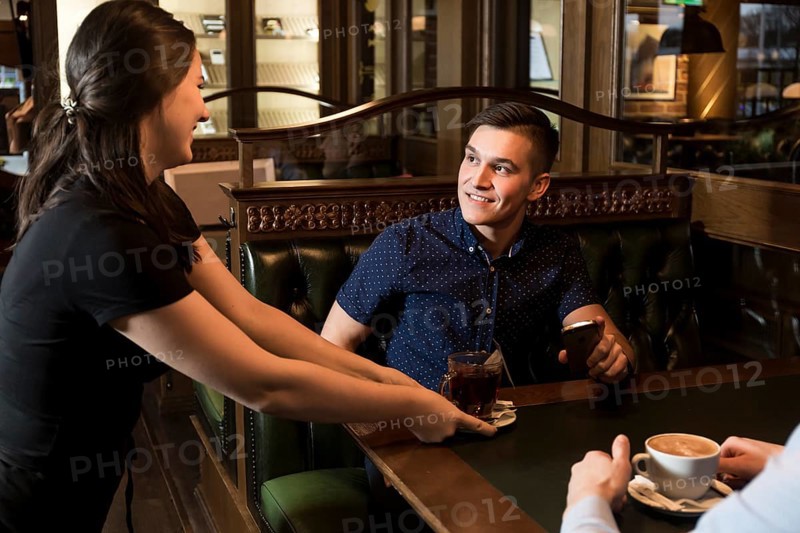 Cheerful waitress serving tea handsome man
