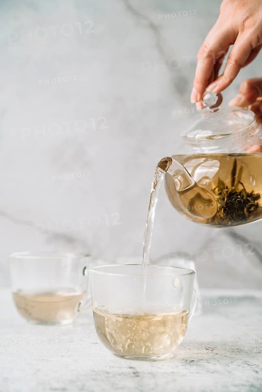 Person pouring tea cups marble background