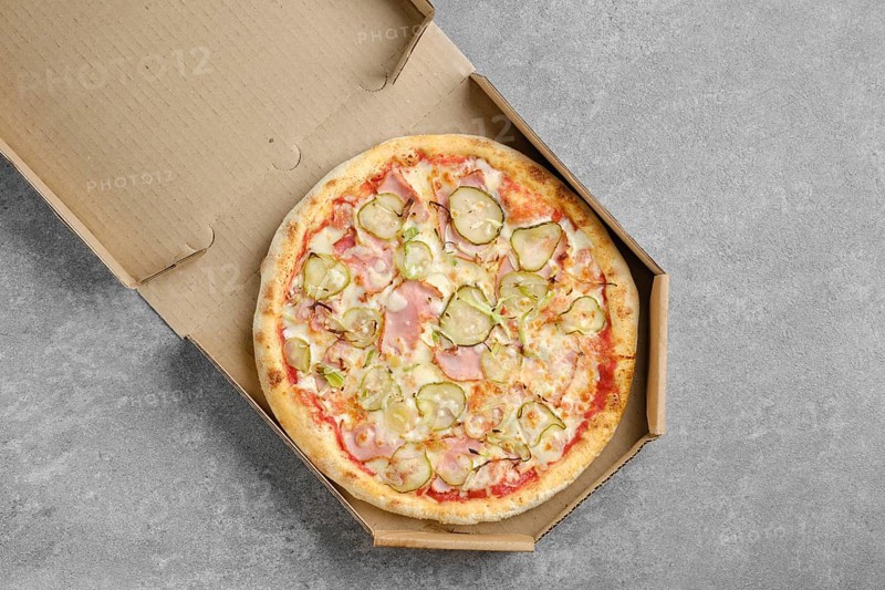 Top view of pizza with ham and pickled cucumber in takeaway cardboard box