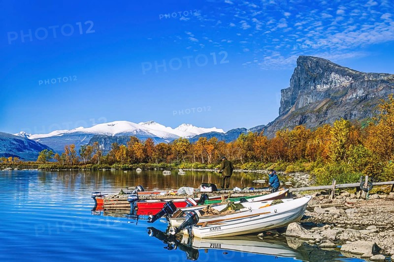 Boats on the lakeshore of a mountain lake with people in autumn at Sarek national park in Sweden