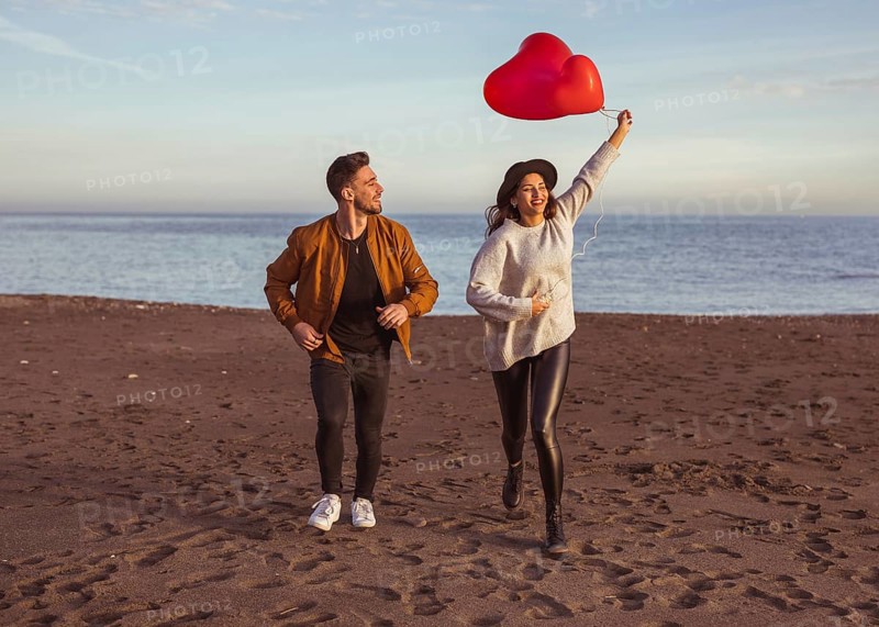 Happy couple running sea shore with heart balloons