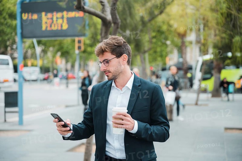 Young businessman holding disposable coffee cup looking mobile phone
