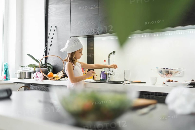 Girl with chef hat washing her hand faucet home
