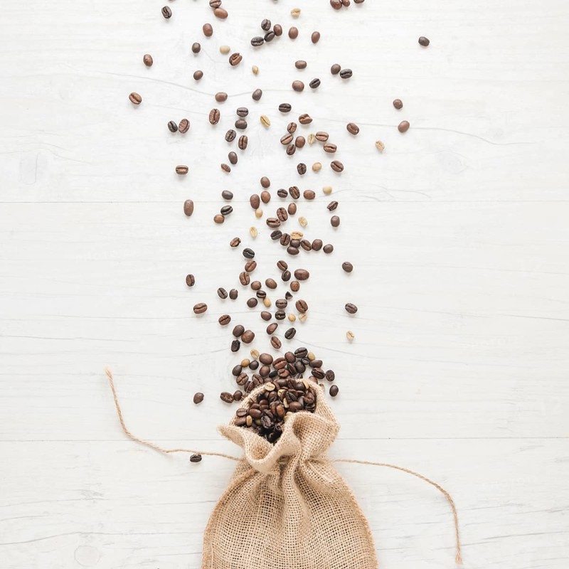 Raw roasted coffee beans falling from small sack desk