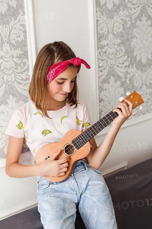 Smiling little girl playing ukulele home