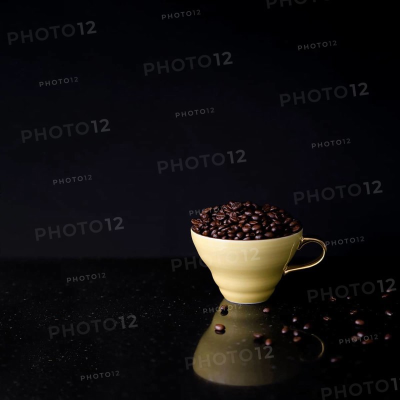 Ceramic cup filled with roasted coffee beans black background