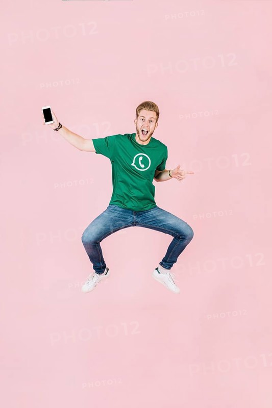 Excited man with smartphone jumping pink backdrop