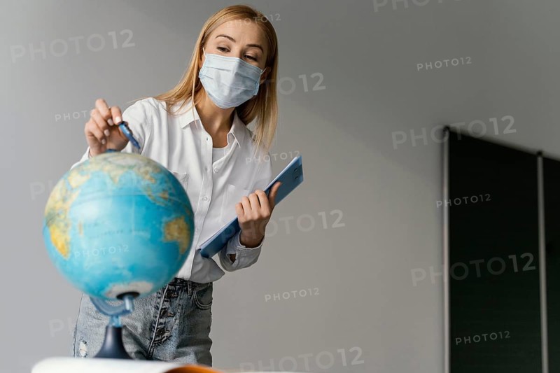 Female teacher classroom with clipboard pointing globe