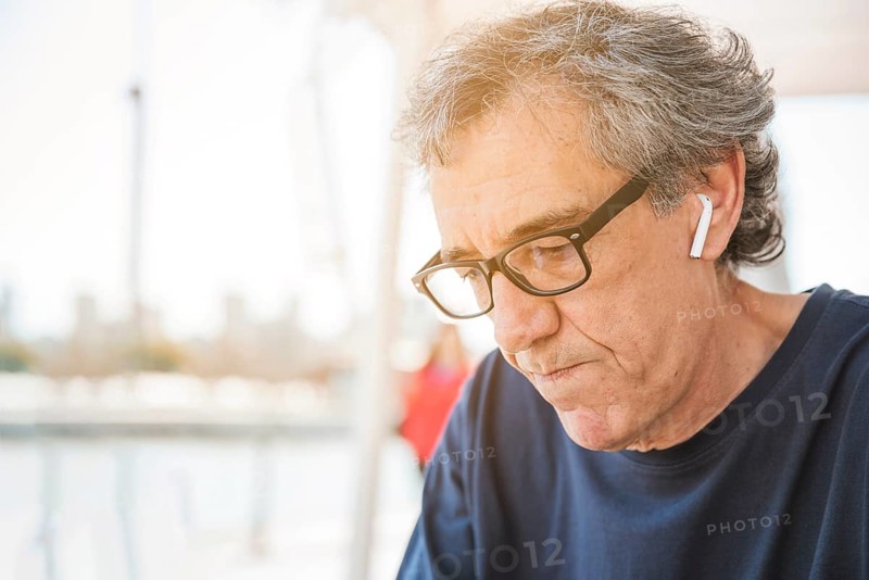 Senior man wearing eyeglasses with white bluetooth earphone his ear
