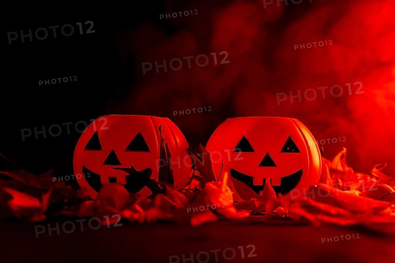 Detail of Halloween pumpkins on autumn leaves with smoke on a red background