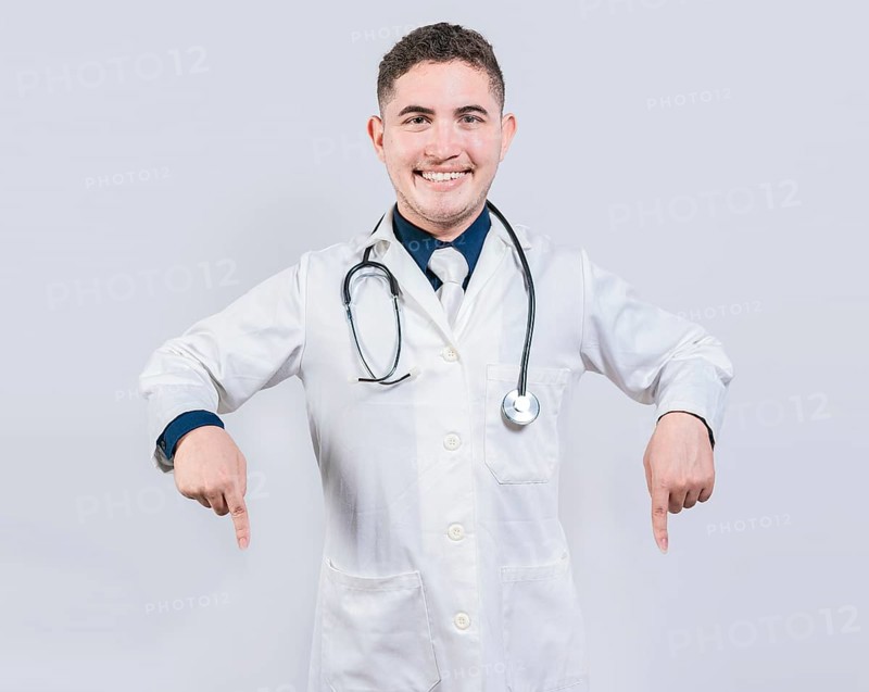 Young doctor pointing a promotion down. Happy doctor pointing fingers down. Latin doctor pointing down an isolated advertising space