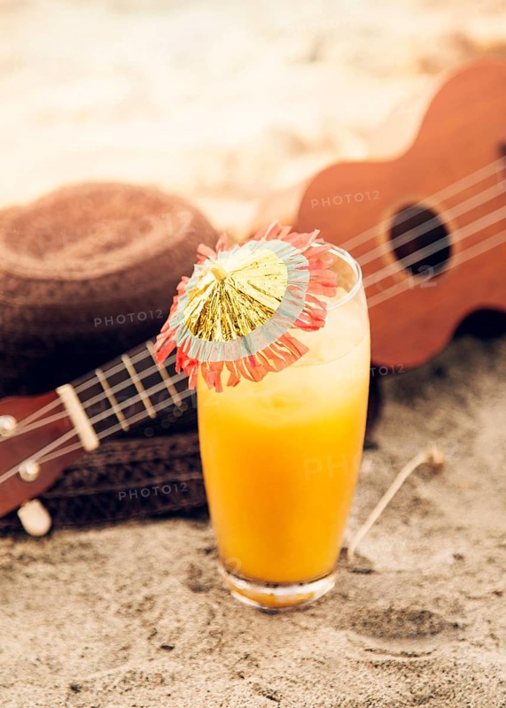 Glass with drink ukulele straw hat placed sand