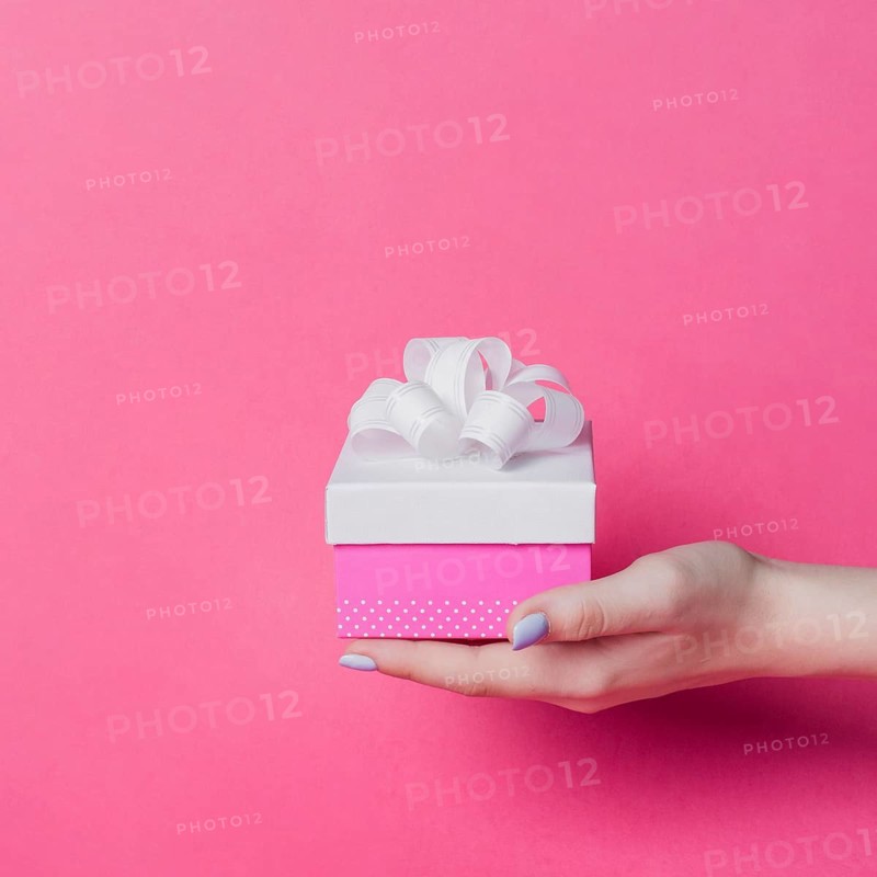 Female s hand holding box with white ribbon bow pink background