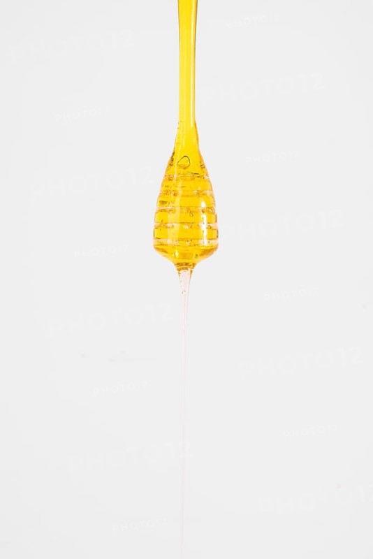 Close up honey dripping from dipper white background