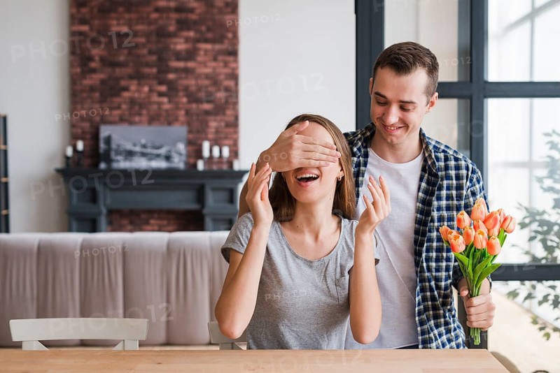 Man with flowers surprising cheerful woman