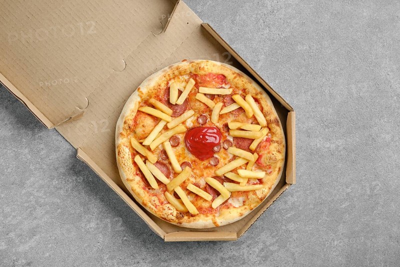 Top view of pizza with various sausages and french fries in cardboard box