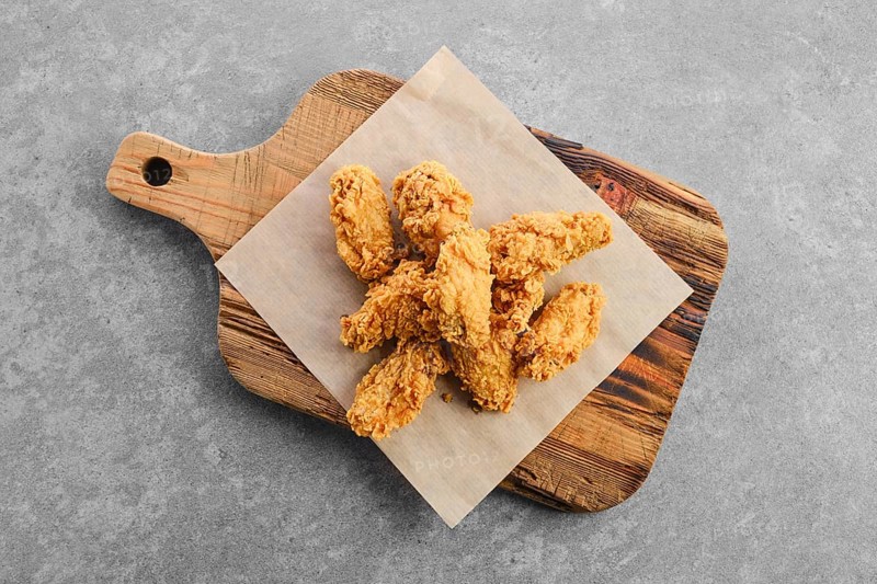 Top view of deep fried chicken wings in breading on wooden serving board