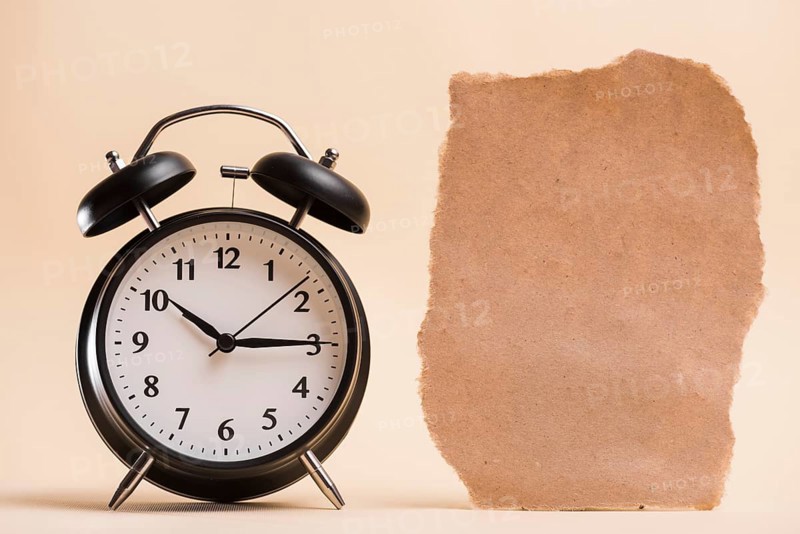 Blank brown torn paper near black alarm clock against colored backdrop