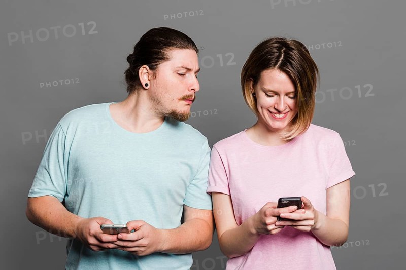 Young man spying peeking smartphone her girlfriend using mobile phone