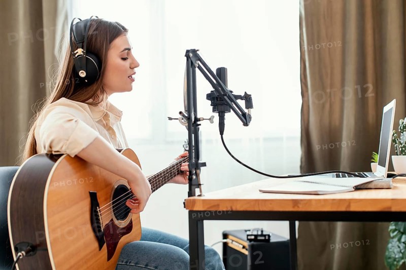Female musician recording song home while playing acoustic guitar