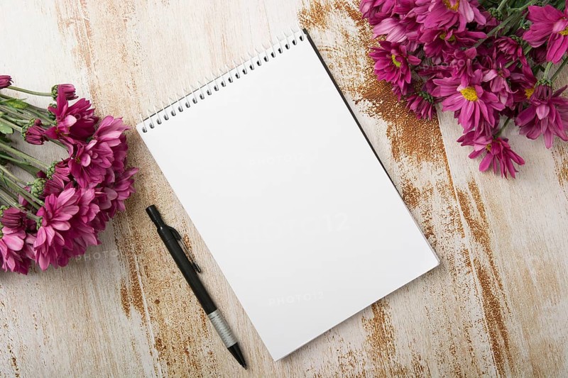 Overhead view spiral notepad with pen pink flowers wooden background