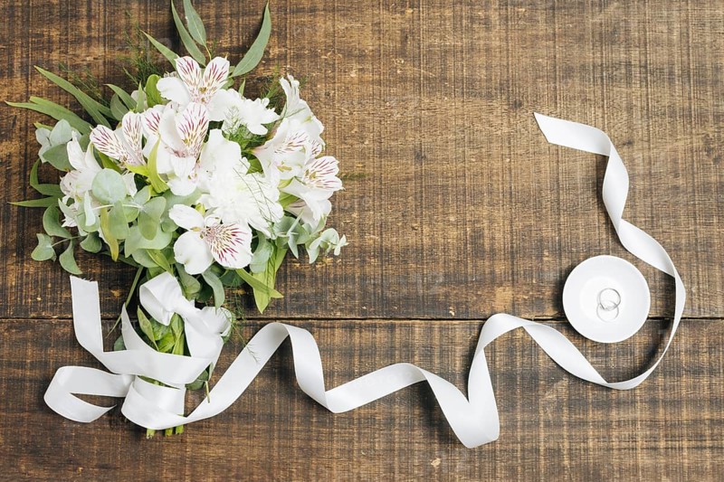 White ribbon flower bouquet with wedding rings plate wooden desk