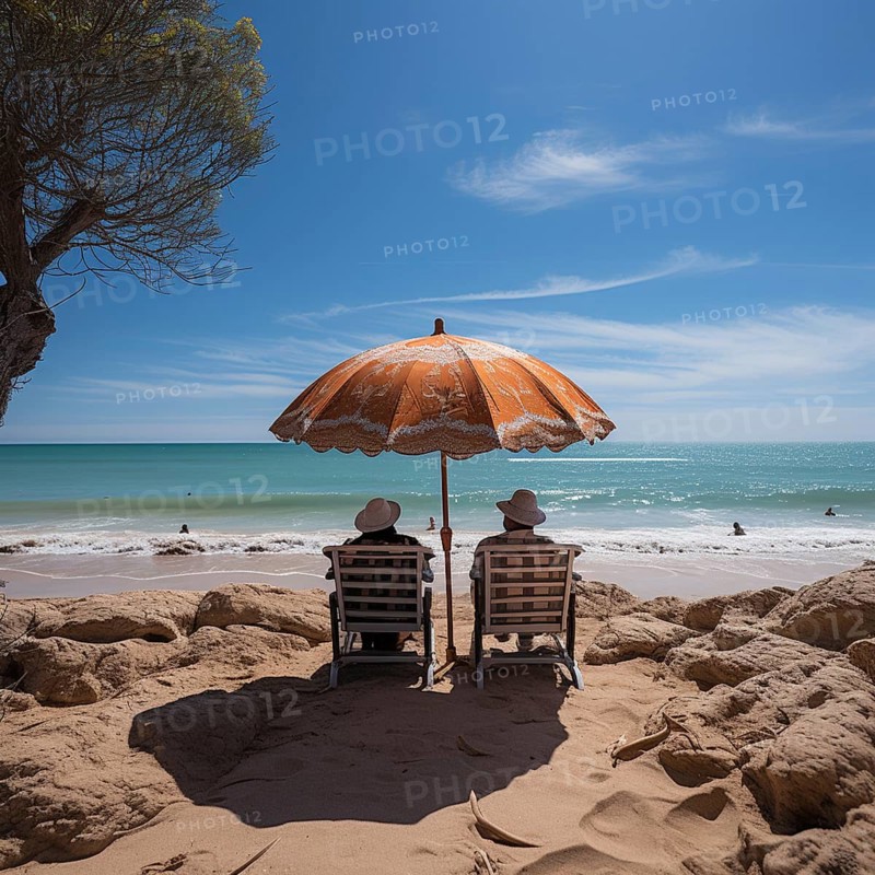 Retired couple sitting on sun loungers under an umbrella and looking at the sea
