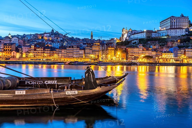 View over the traditional Rabelo boats on the Douro riverbank in Vila Nova de Gaia towards the old town of Porto at dusk