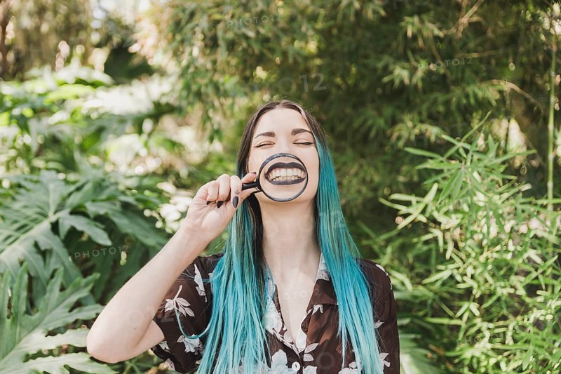 Young woman holding magnifying glass front her mouth