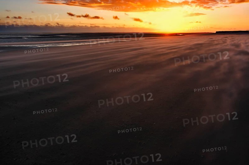 Sand drifting on the beach of the island of Minsener Oog at sunset