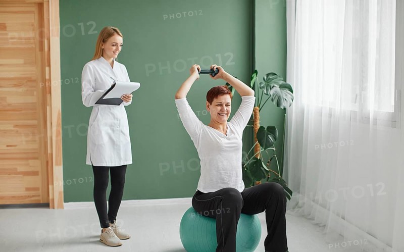 Elder woman covid recovery doing physical exercises with dumbbell while nurse checks