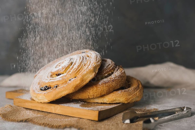 Close up sugar dusting baked cinnamon buns chopping board