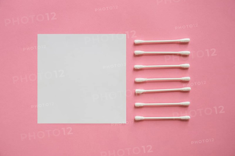 Row cotton swabs near blank adhesive note pink background