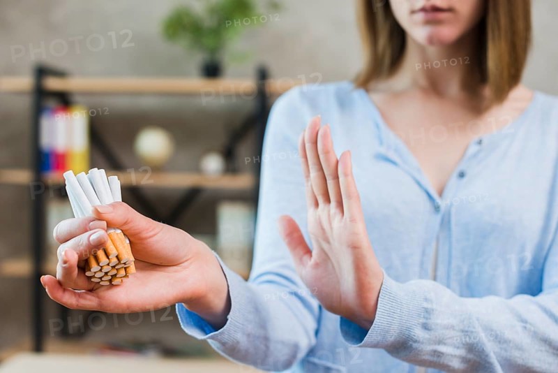 Woman showing stop gesture holding bunch cigarettes hand