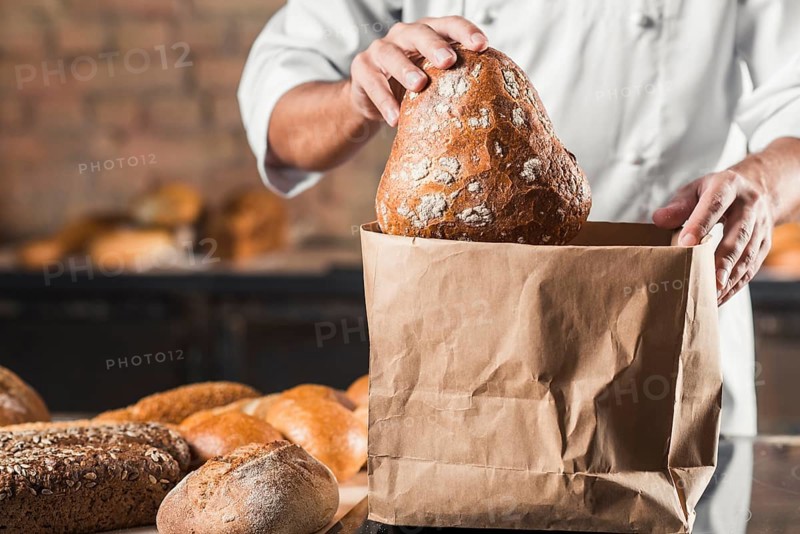 Male baker putting baked bread brown paper bag