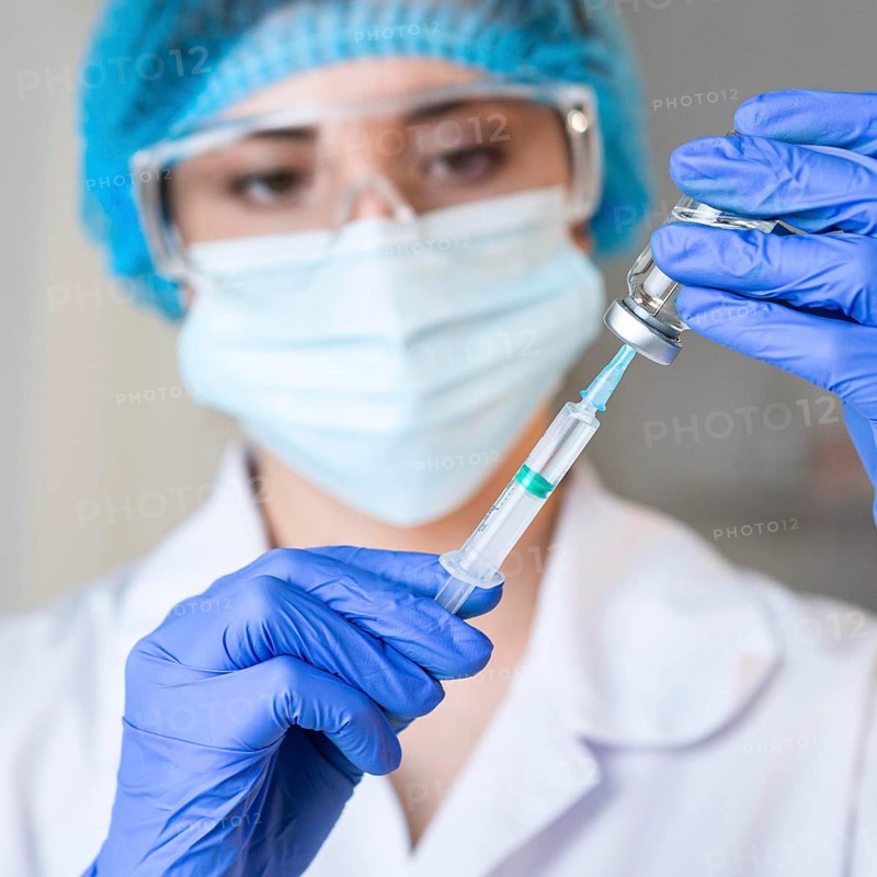 Female researcher with safety glasses medical mask holding syringe