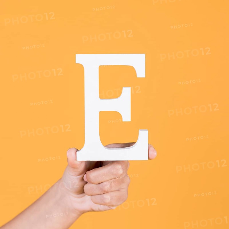 Close up hand holding up uppercase capital letter e yellow background