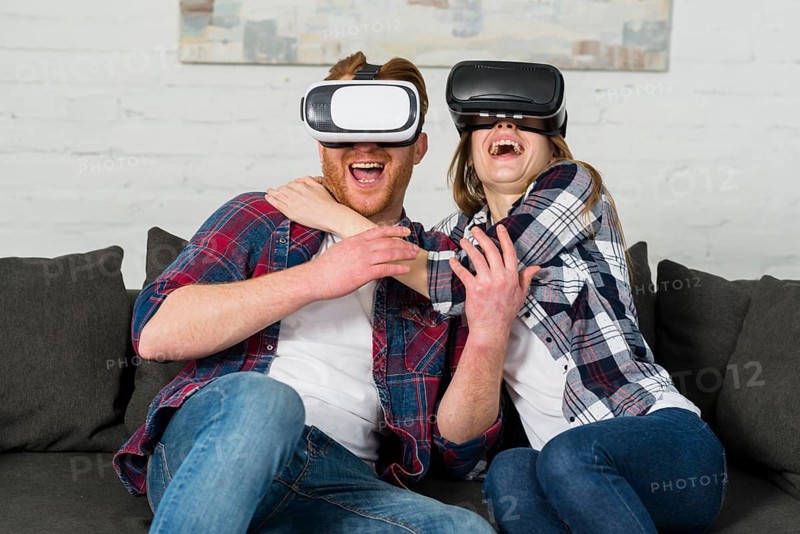 Excited young couple sitting sofa using vr headset experiencing virtual reality