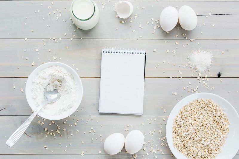 High angle view spiral notepad oats eggs flour milk wooden backdrop
