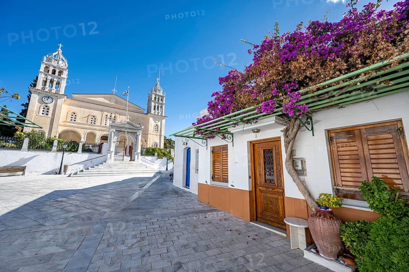 White Cycladic house with purple bougainvillea and Agia Triada church