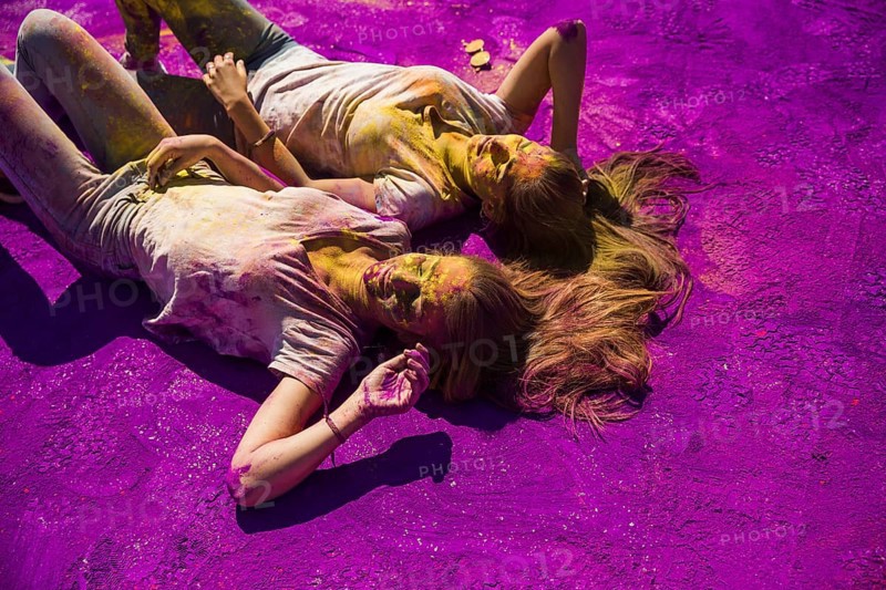 Two young women lying side by side purple holi powder