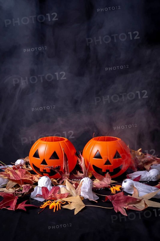 Halloween pumpkins over red autumn leaves and ghosts with smoke on a black background