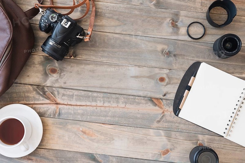 Top view dslr camera cup tea spiral notepad pen camera lens bag wooden table