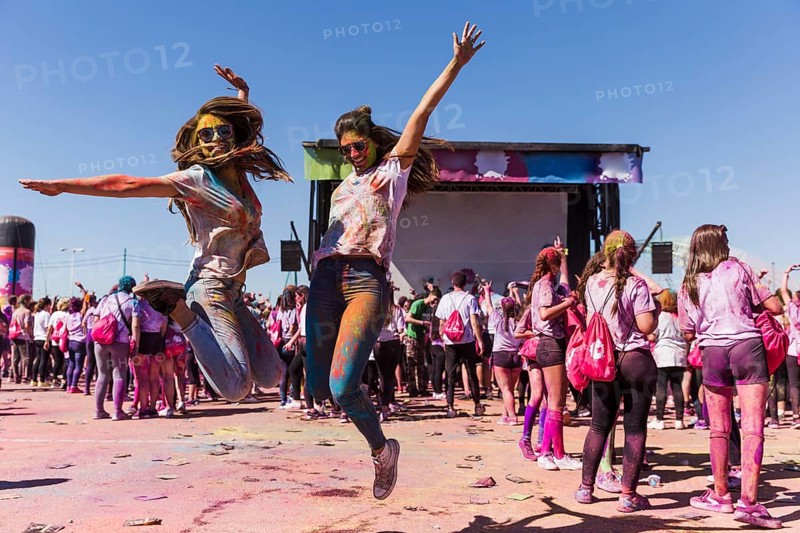 Excited young women jumping air celebrating holi festival