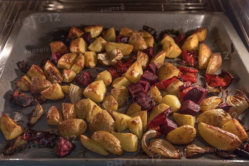 Vegetables and jacket potatoes on a baking tray in the oven
