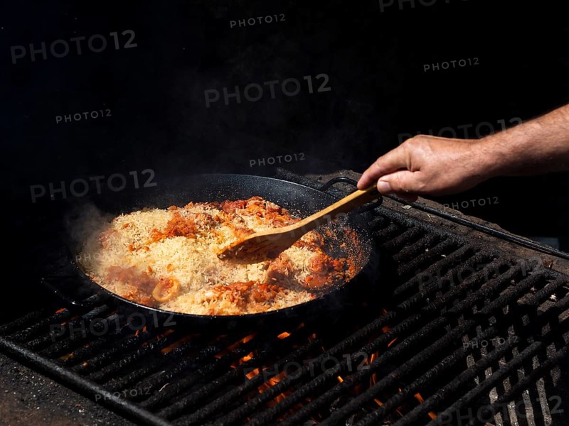 Cook mixing rice with calamari rings vegetables frying pan