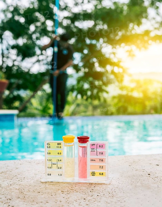 Water PH tester kit on the edge of the swimming pool with maintenance person in the background