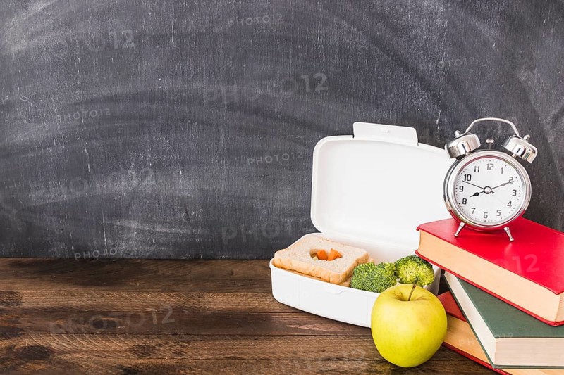 Lunchbox apple near books alarm clock