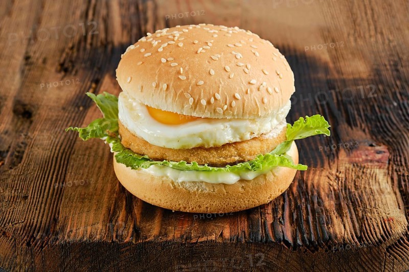 Chicken burger with fried egg and fresh iceberg lettuce salad on wooden board