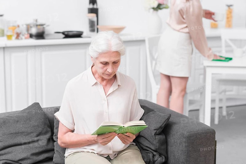 Senior woman sitting sofa reading book home